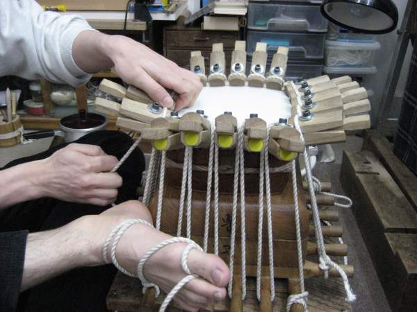 道具と紐を使って三味線の皮を張る作業